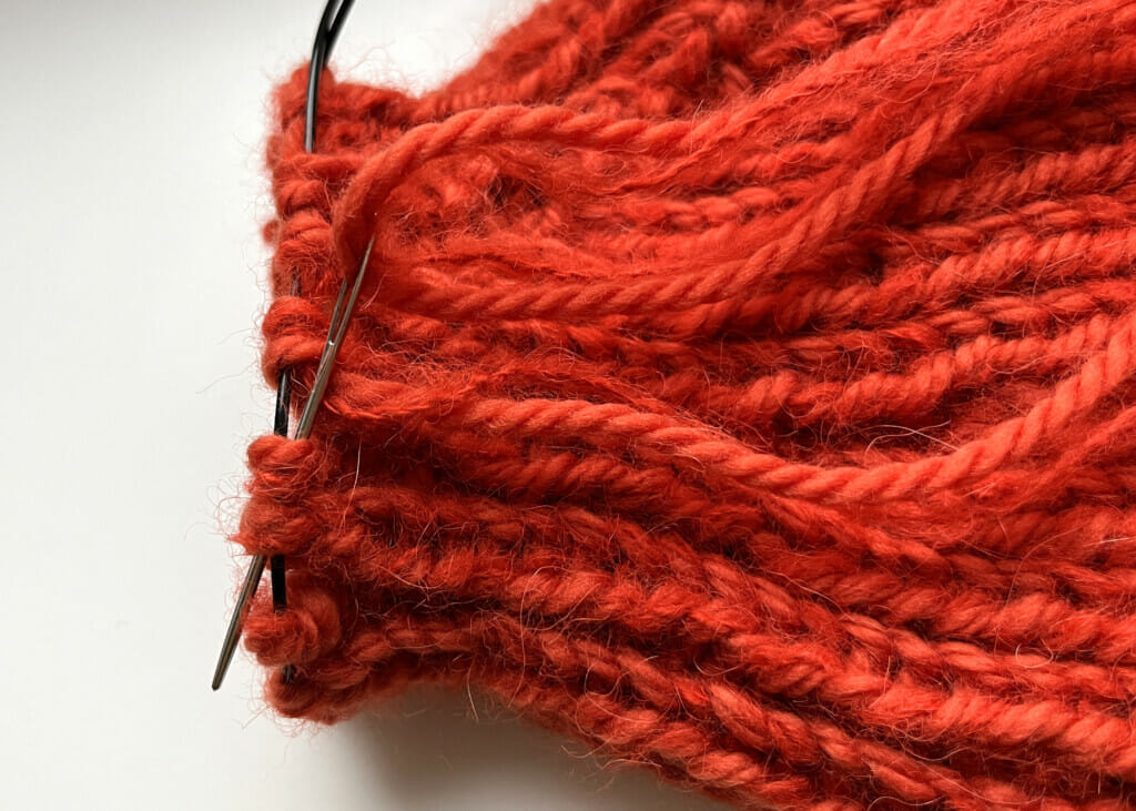 Die Fäden der gestrickten Mütze werden zum Schluss mit Wollnadeln kreisförmig vernäht.